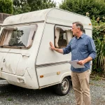 Un particulier examinant une caravane d'occasion blanche garée dans une allée résidentielle, document en main
