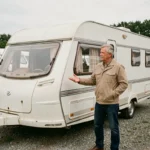 Homme inspectant une caravane d'occasion blanche dans un parc de vente de véhicules de loisirs d'occasion