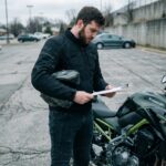 Motard tenant des documents d'assurance moto à côté d'une Kawasaki Z900, illustrant le changement d'assurance lors du passage du permis A2 au permis A