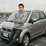 Jeune homme appuyé contre une voiture sans permis de style JDM dans un parking urbain